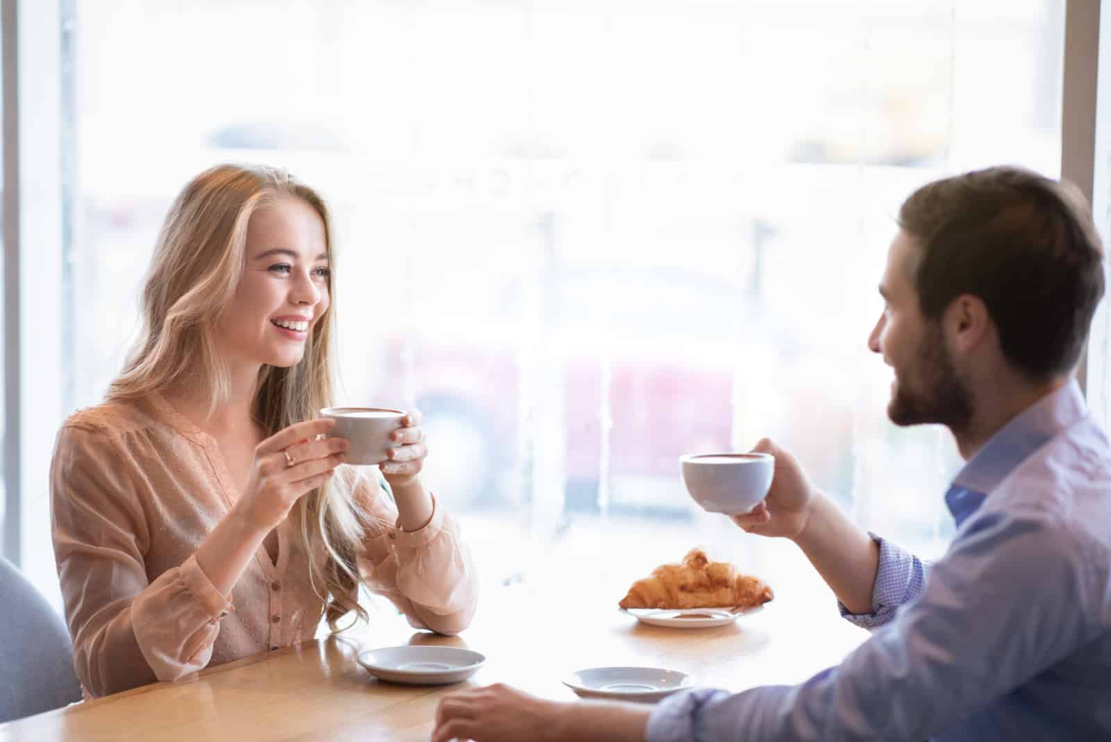 un hombre y una mujer sonrientes se sientan a la mesa y charlan tomando un café