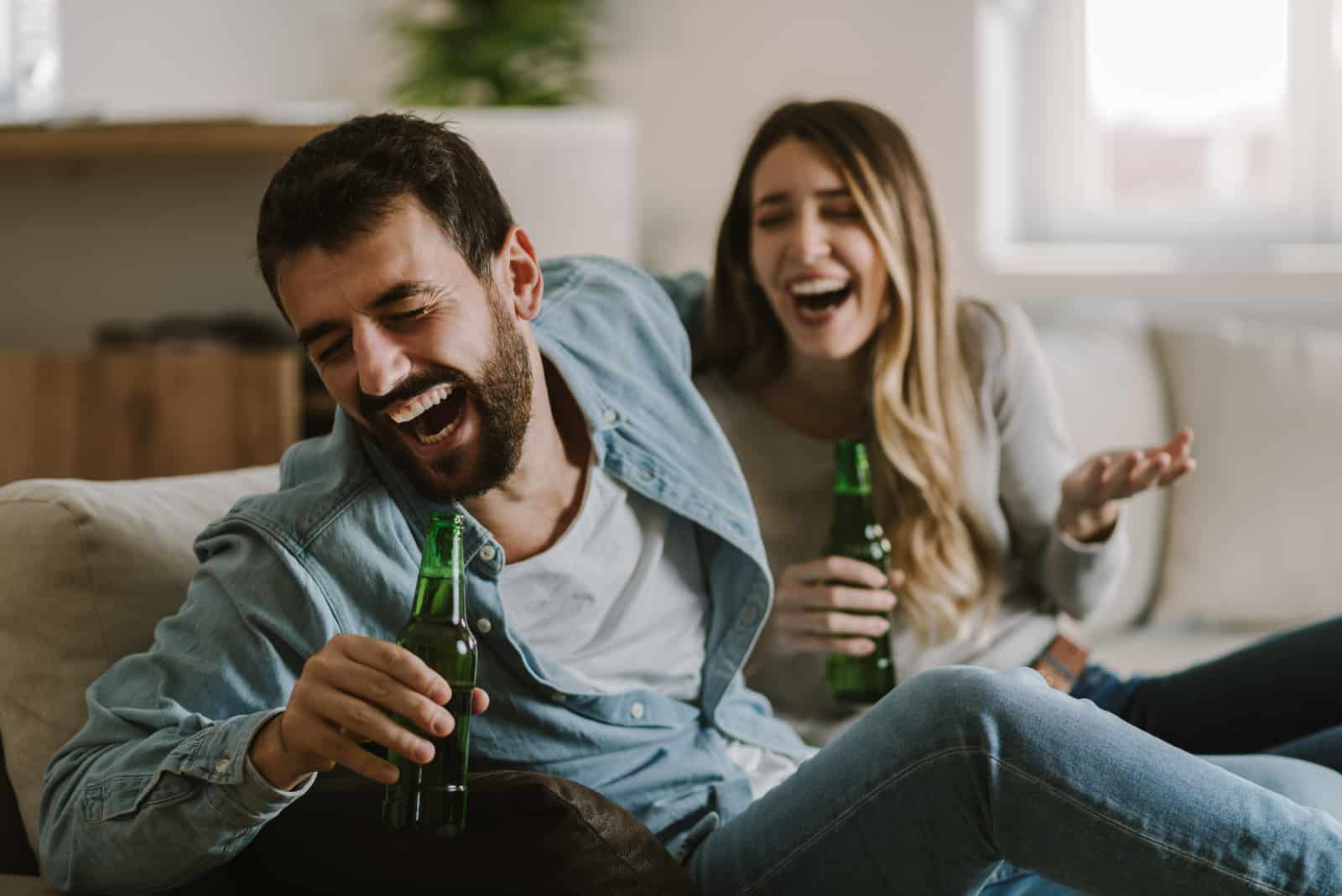 un uomo e una donna sorridenti seduti sul divano a bere birra