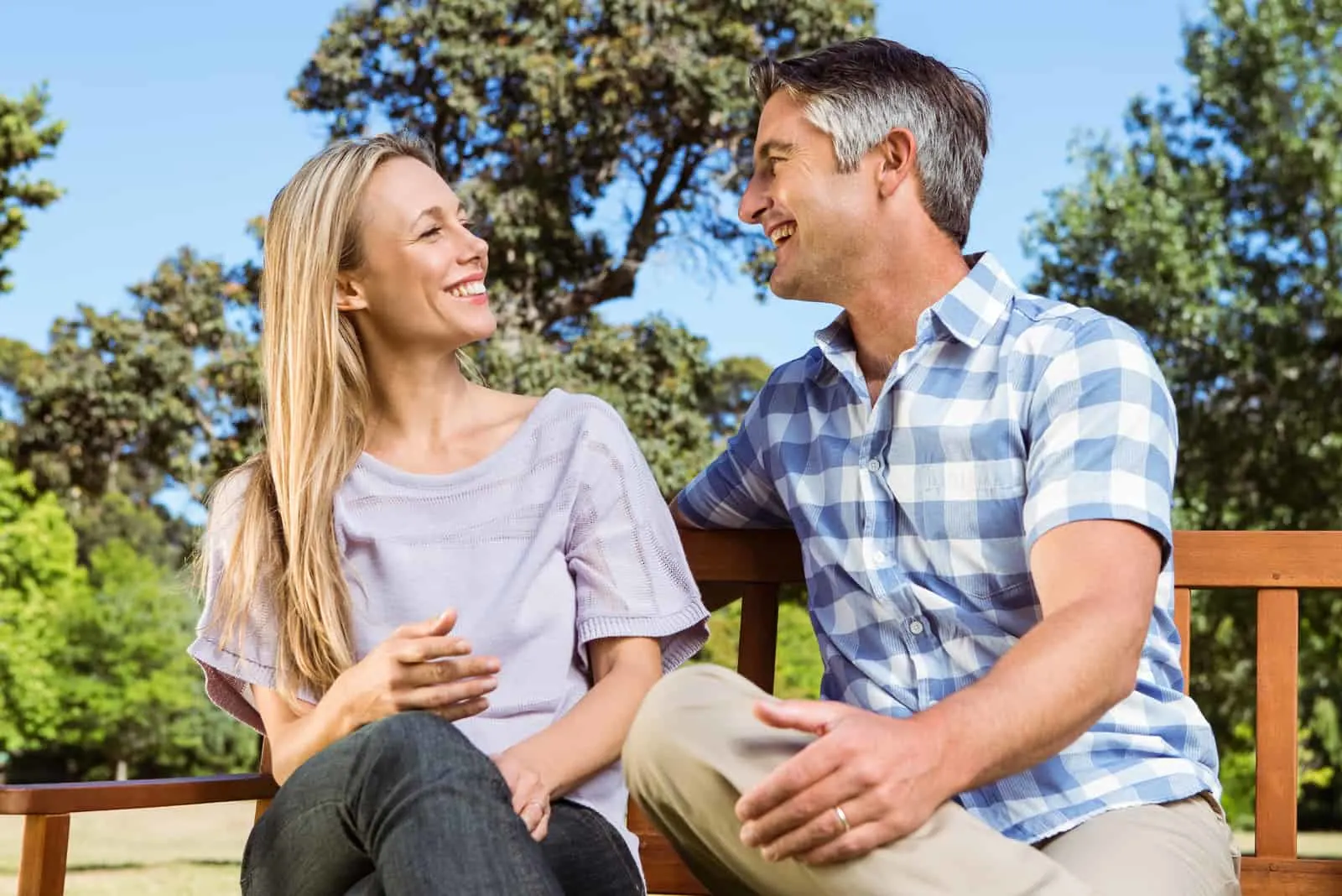 a smiling man and woman talking on a bench