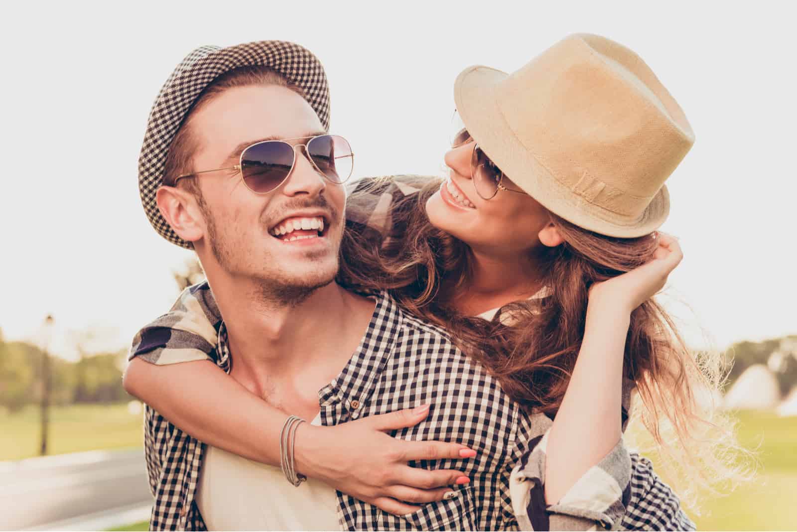 un uomo sorridente porta in braccio una donna con un cappello in testa