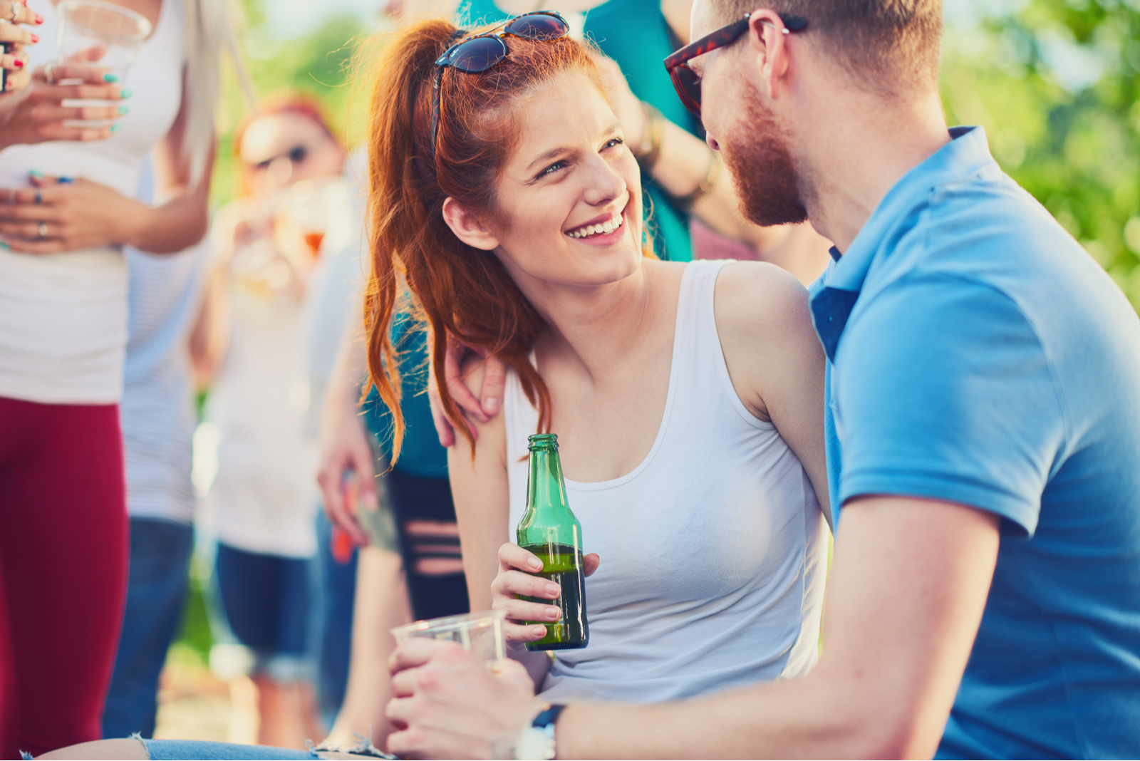 una mujer sonriente sostiene una cerveza en la mano y habla con un hombre