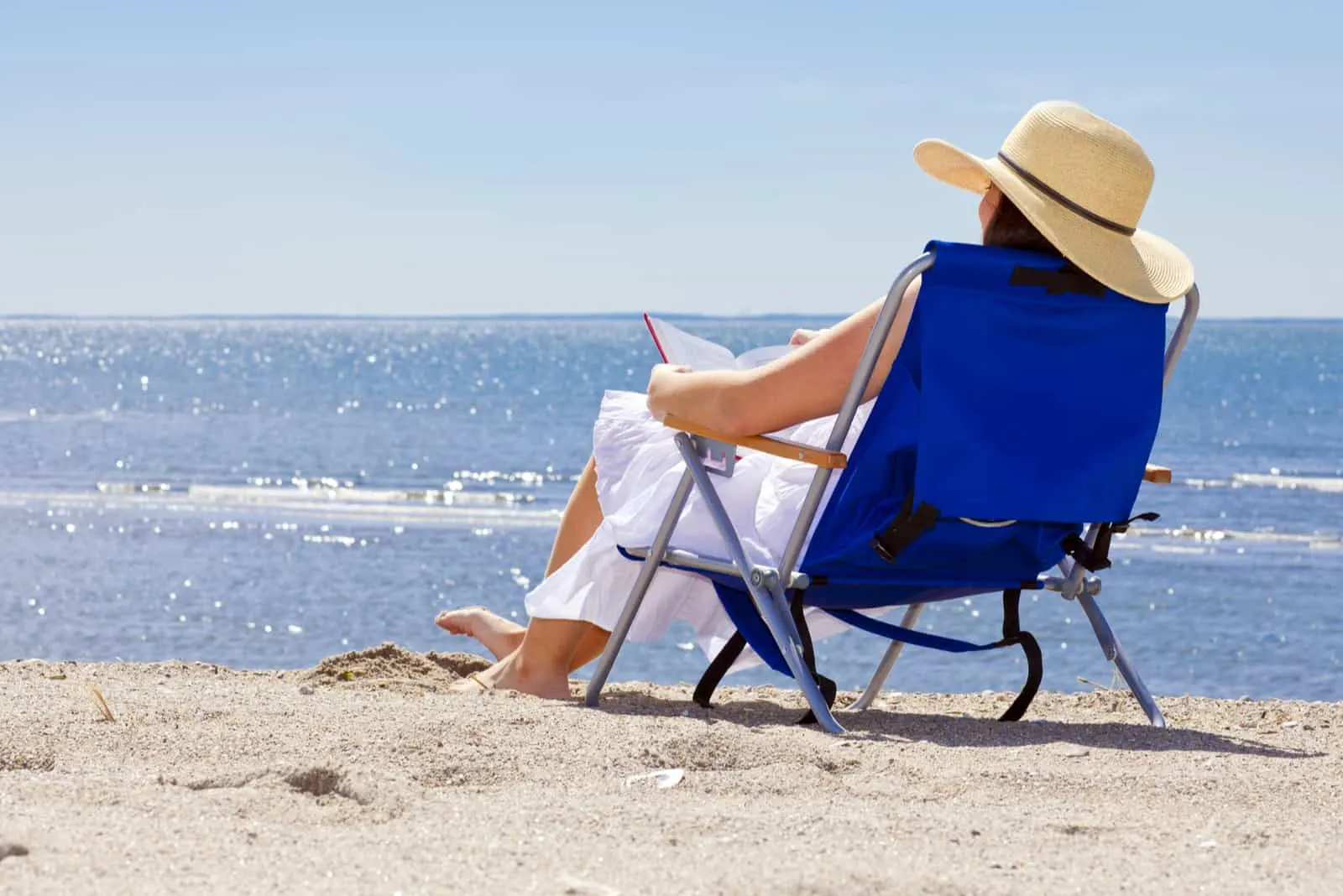 a woman with a hat on her head is lying in a deck chair reading a book