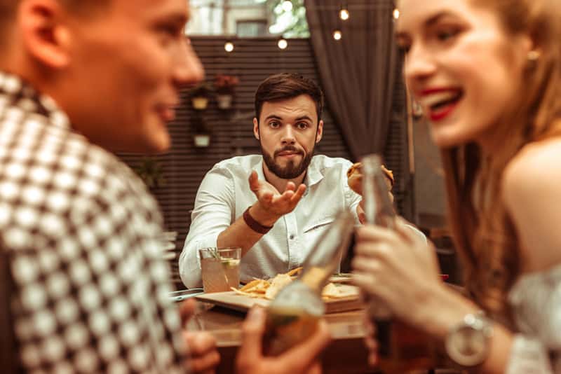 Uomo infastidito che guarda la sua ragazza mentre brinda con un amico maschio in un ristorante
