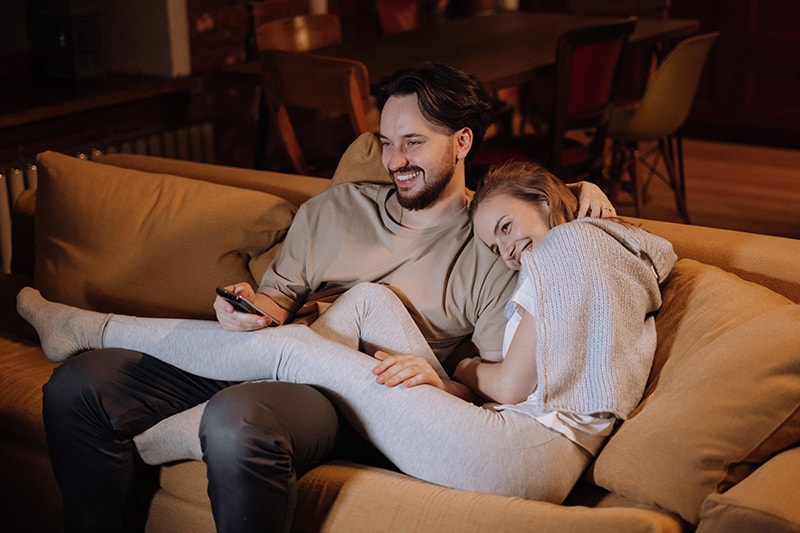 casal alegre sentado no sofá, à noite, em casa