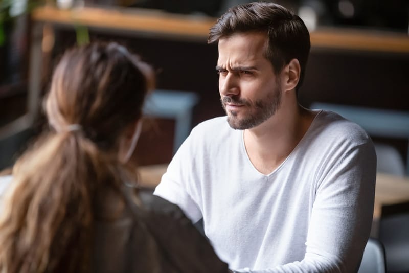 confused man looking at a woman sitting with him in cafe
