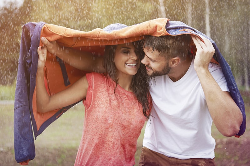 coppia romantica che si nasconde dalla pioggia sotto la giacca