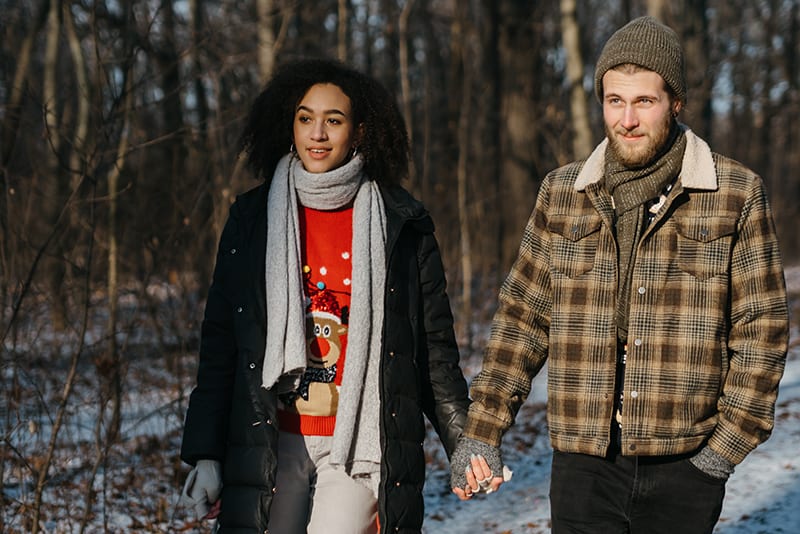 couple holding hands while walking in the wood in winter