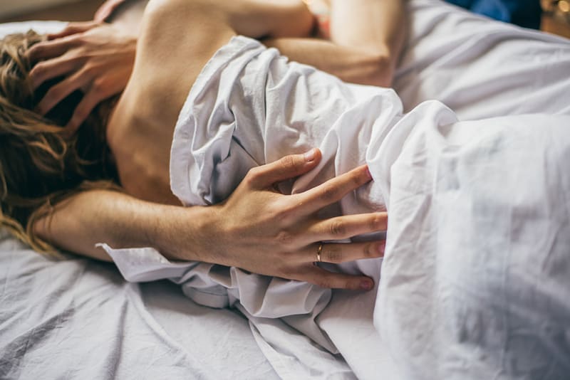 coppia che si bacia nel letto sotto le lenzuola bianche