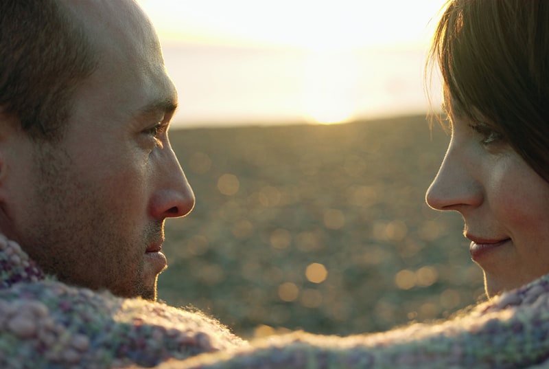 couple looking at each other wrapped in blanket on beach