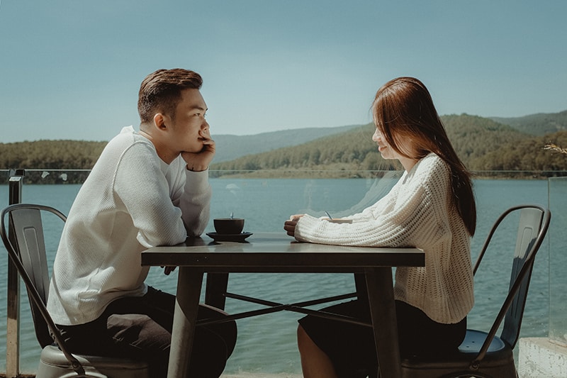 couple sitting beside lake drinking coffee