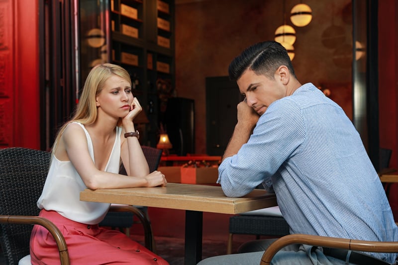 distracted man sitting with sad girl in cafe on a date