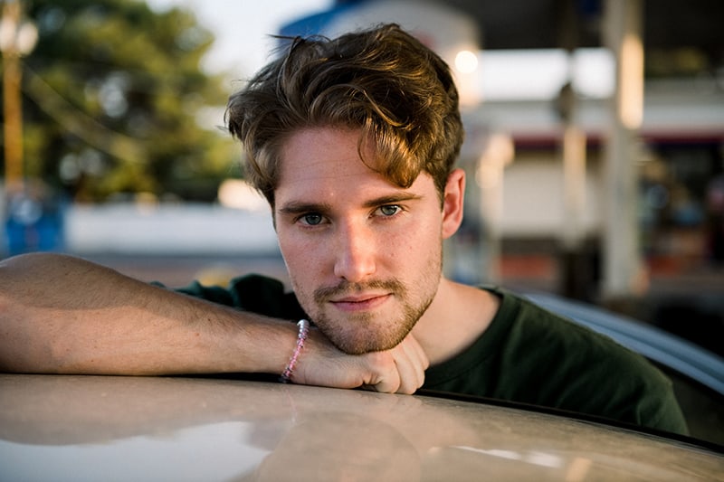 handsome man with blue eyes leaning on the car