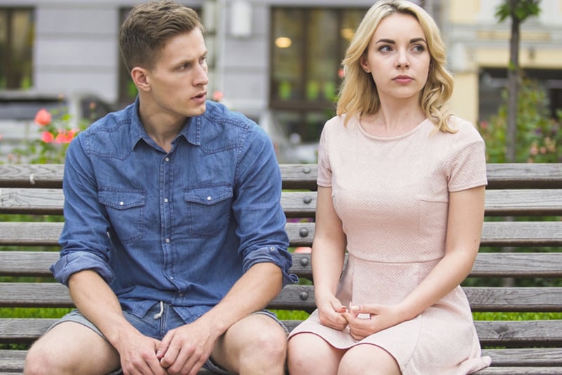 jealous man looking at his upset girlfriend sitting on the bench next to him