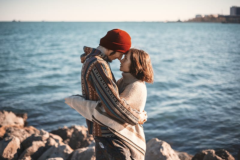 man and woman hugging while standing on the rocks near the sea