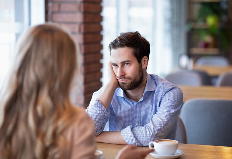 hombre sintiendose mal mientras escucha a una mujer sentada con el en el cafe