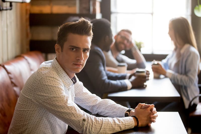 hombre sintiendo celos sentado separado de sus amigos en un cafe