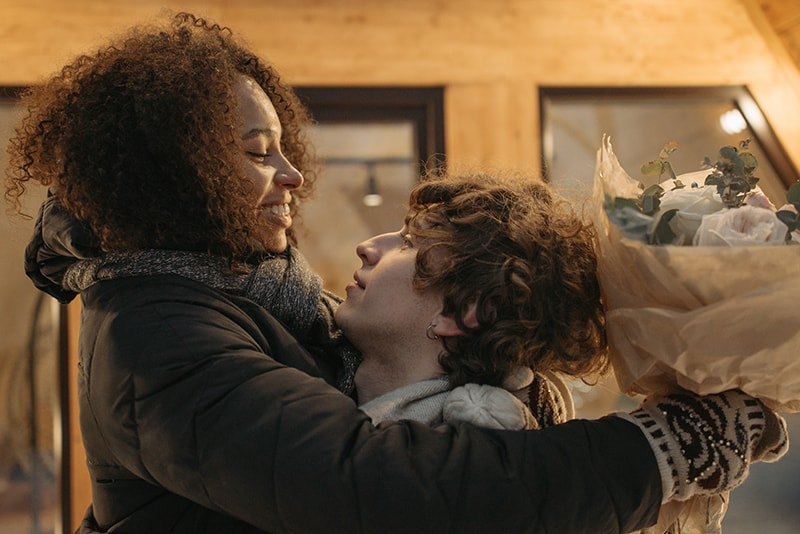 man lifting his smiling girlfriend holding bouquet of flowers