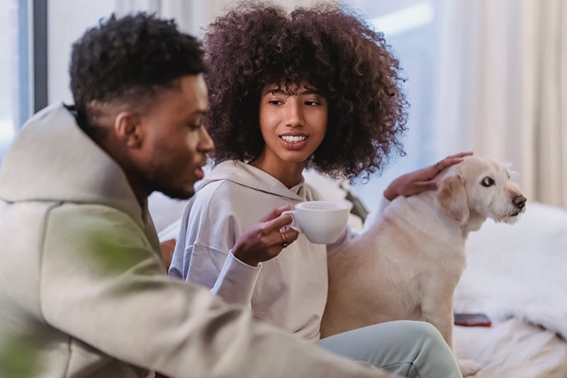 man talking with his girlfriend holding cup of coffee and storing dog