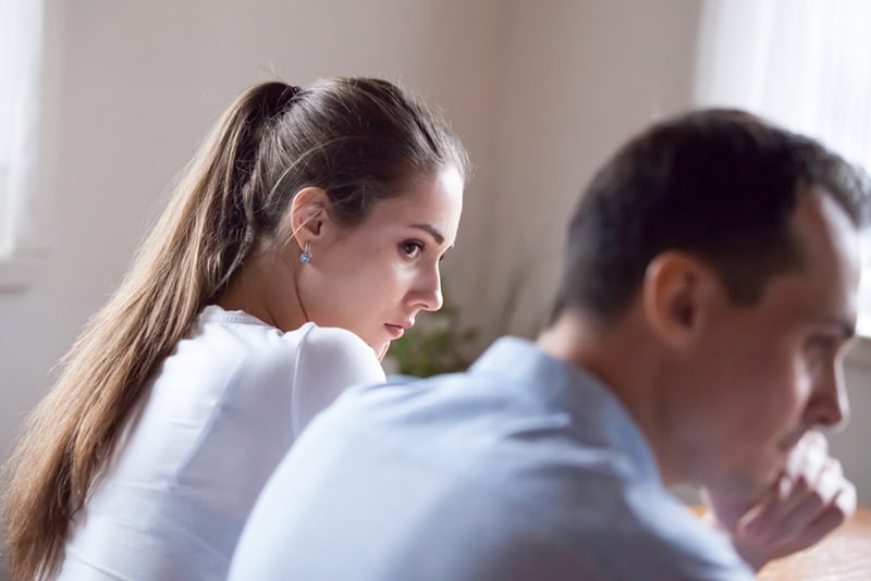 serious woman looking at upset boyfriend sitting close to her