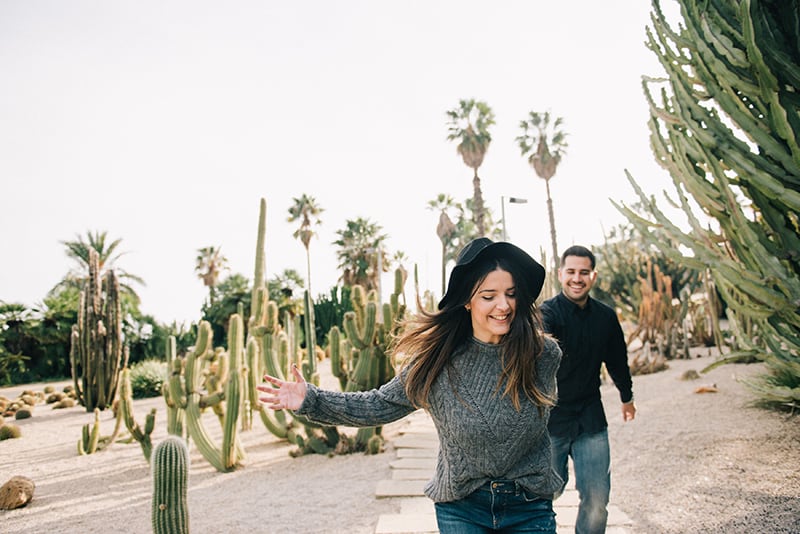 smiling couple holding hands and running near the cactus plants