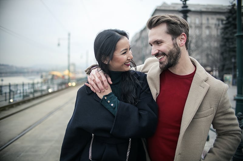 smiling couple looking at each other while walking on sidewalk