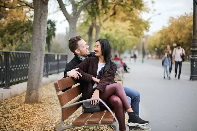 smiling man and woman looking at each other while sitting on the bench