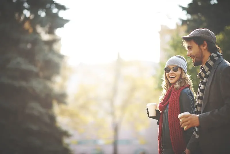 smiling man and woman walking together and drinking coffee