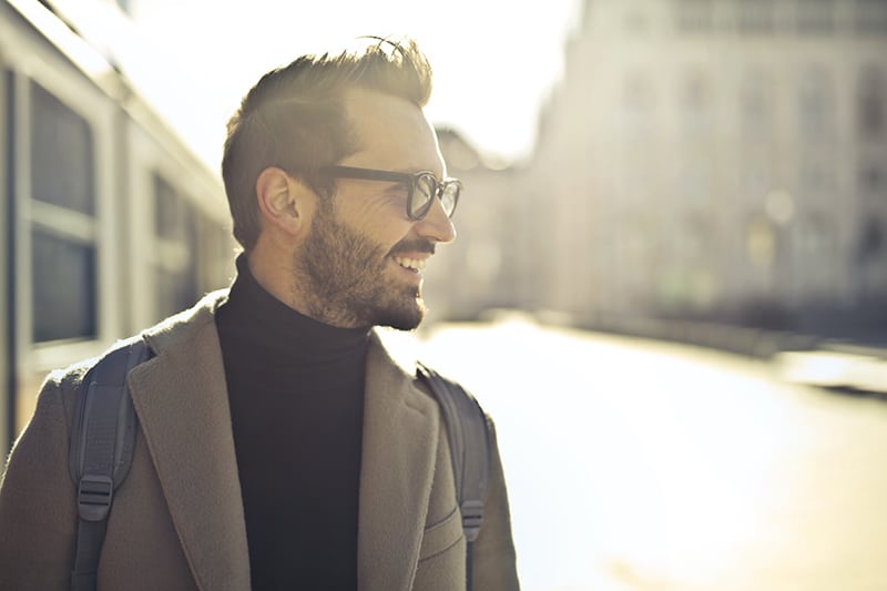 hombre sonriente con gafas mirando a un lado mientras camina por la ciudad