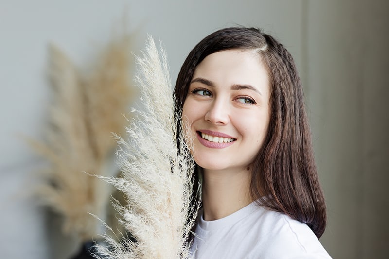 smiling woman holding decorative grass and looking aside