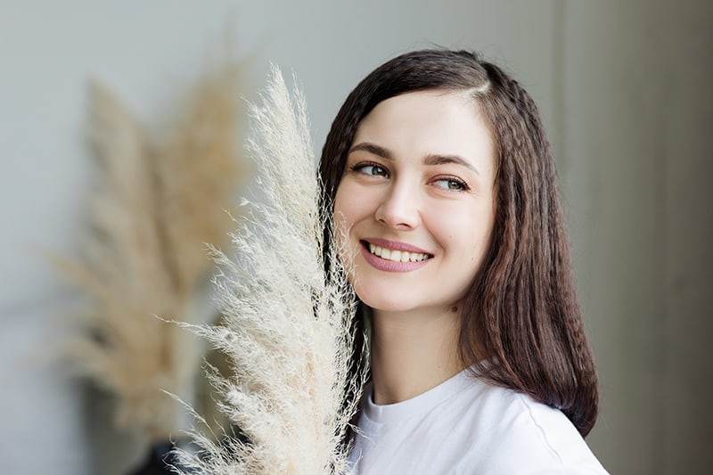 mulher sorridente segurando relva decorativa e olhando para o lado