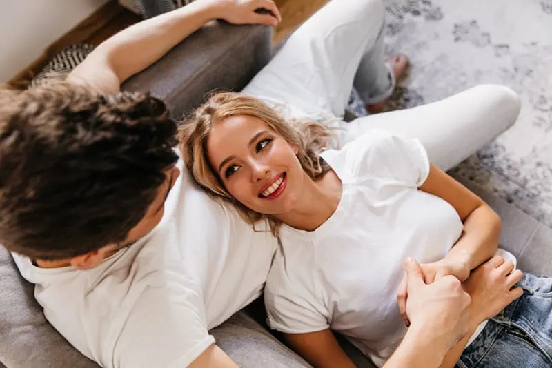 smiling woman looking at her boyfriend while lying in his lap