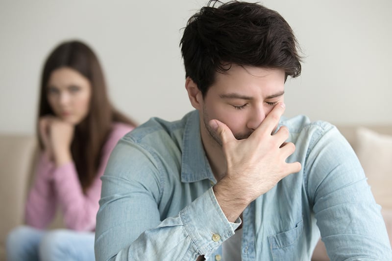 upset man covering face with hand sitting in front of his girlfriend