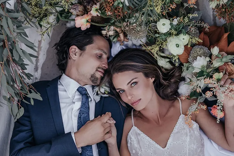 wedding couple holding hands and lying surrounded with flowers