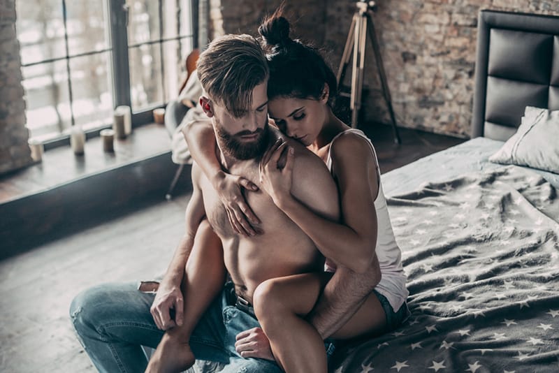 woman embracing a man sitting on the edge of the bed