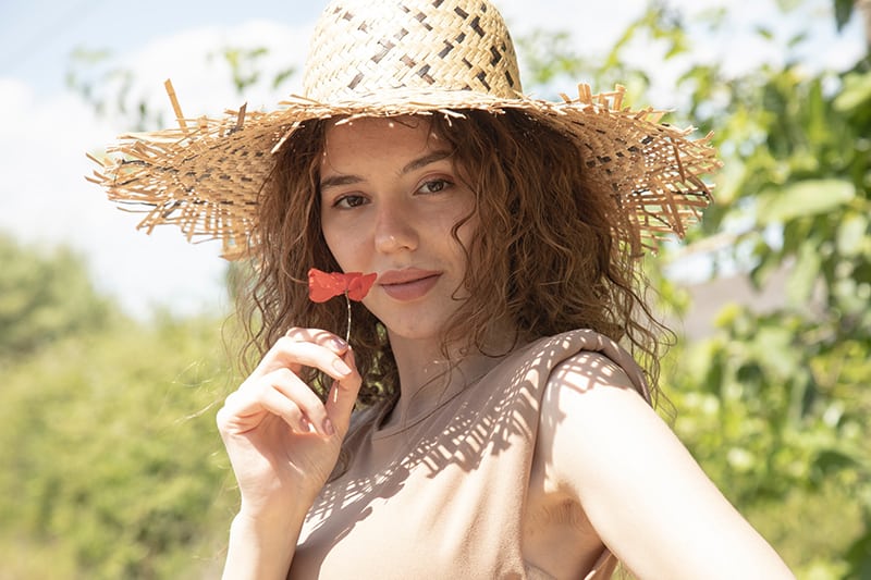 woman in brown sun hat holding red flower