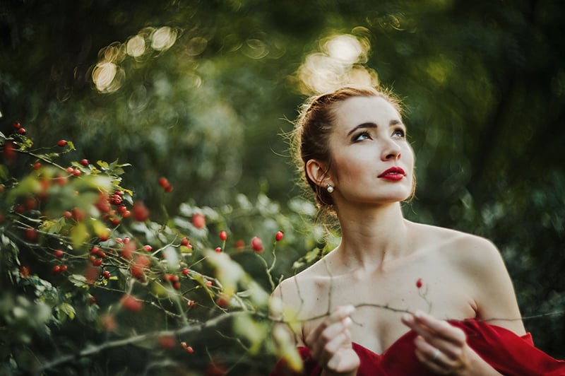 woman in red dress standing near the rosehip and looking up in the sky