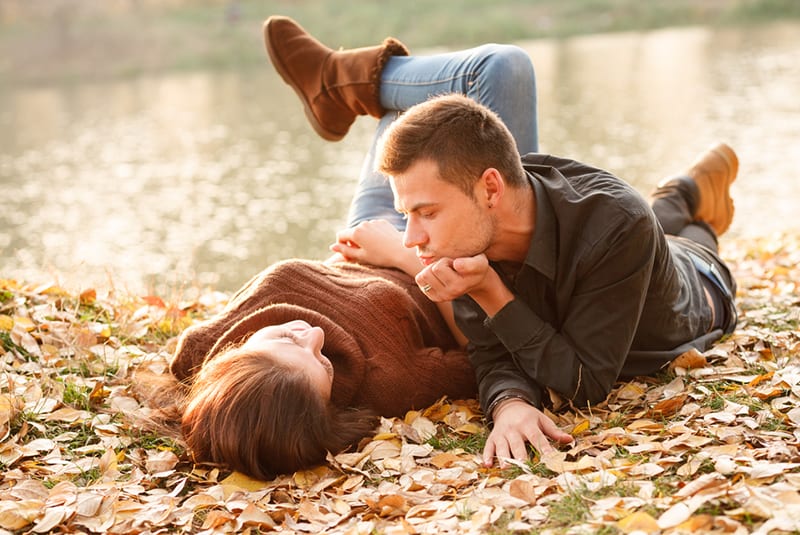 young man and woman lying down near the lake and talking