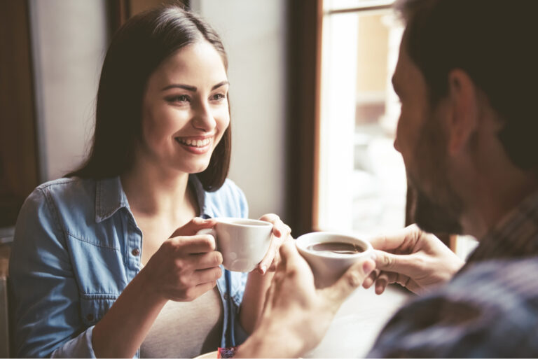 um homem e uma mulher sorridentes sentam-se à mesa e conversam durante um café