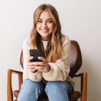 a smiling woman sitting on a chair holding a phone in her hand