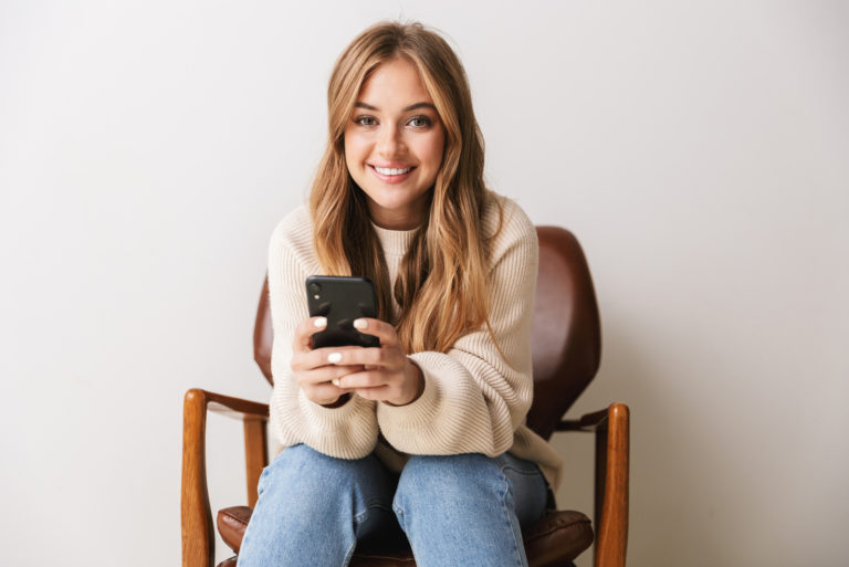a smiling woman sitting on a chair holding a phone in her hand