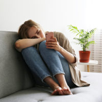 sad girl sitting on couch looking at phone