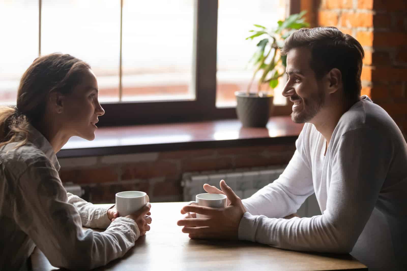 a smiling man and woman sitting at a table having coffee talking