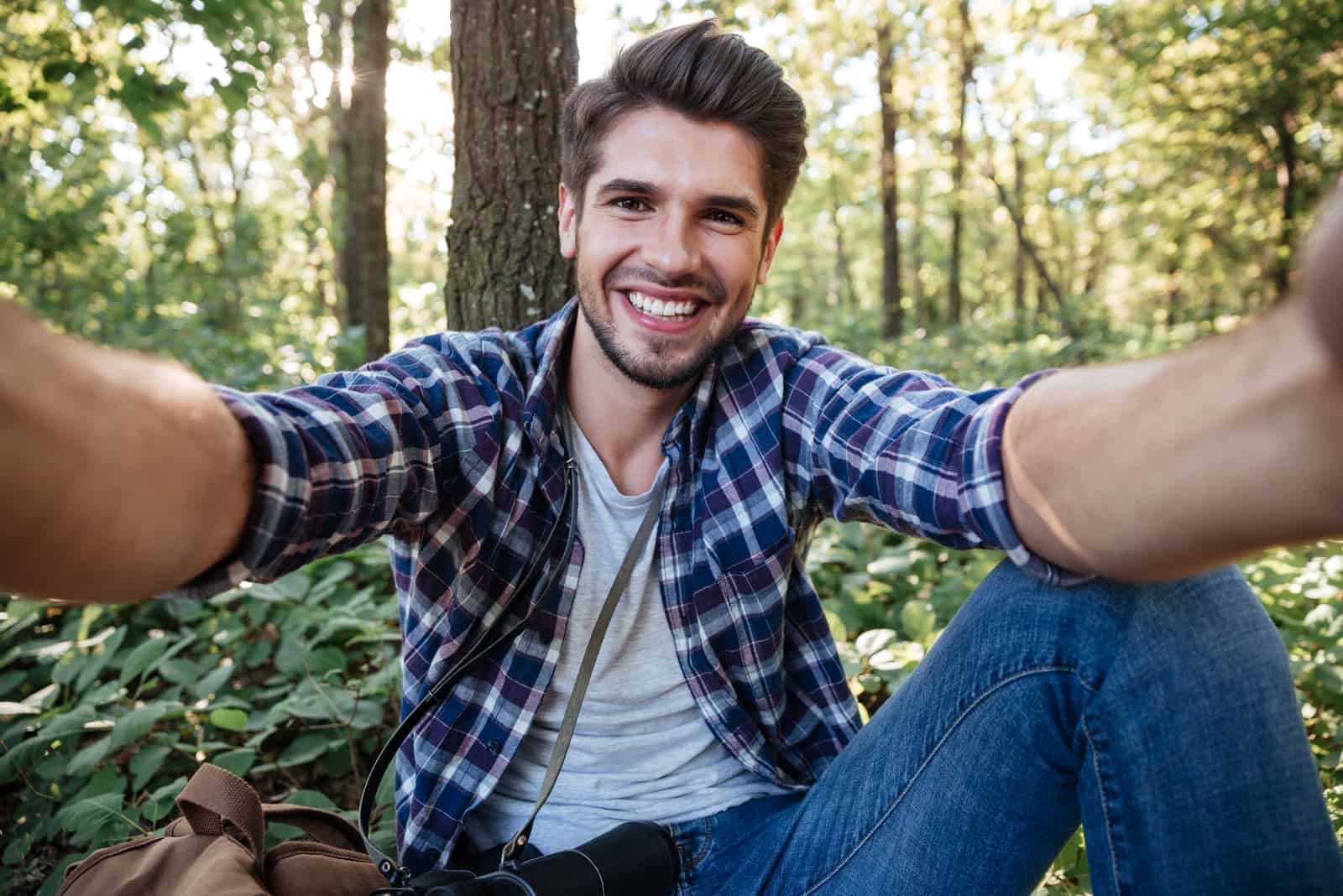 a smiling man sits in the woods and takes a picture