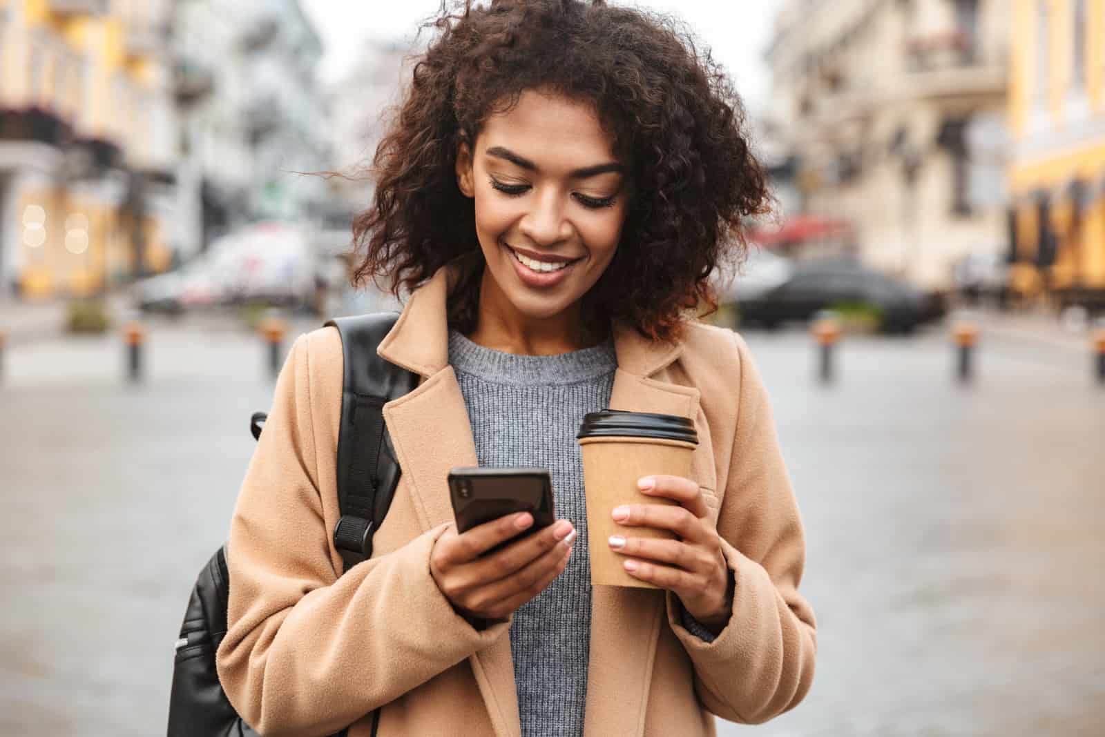 a smiling woman with coffee in her hand stands and a button on the phone
