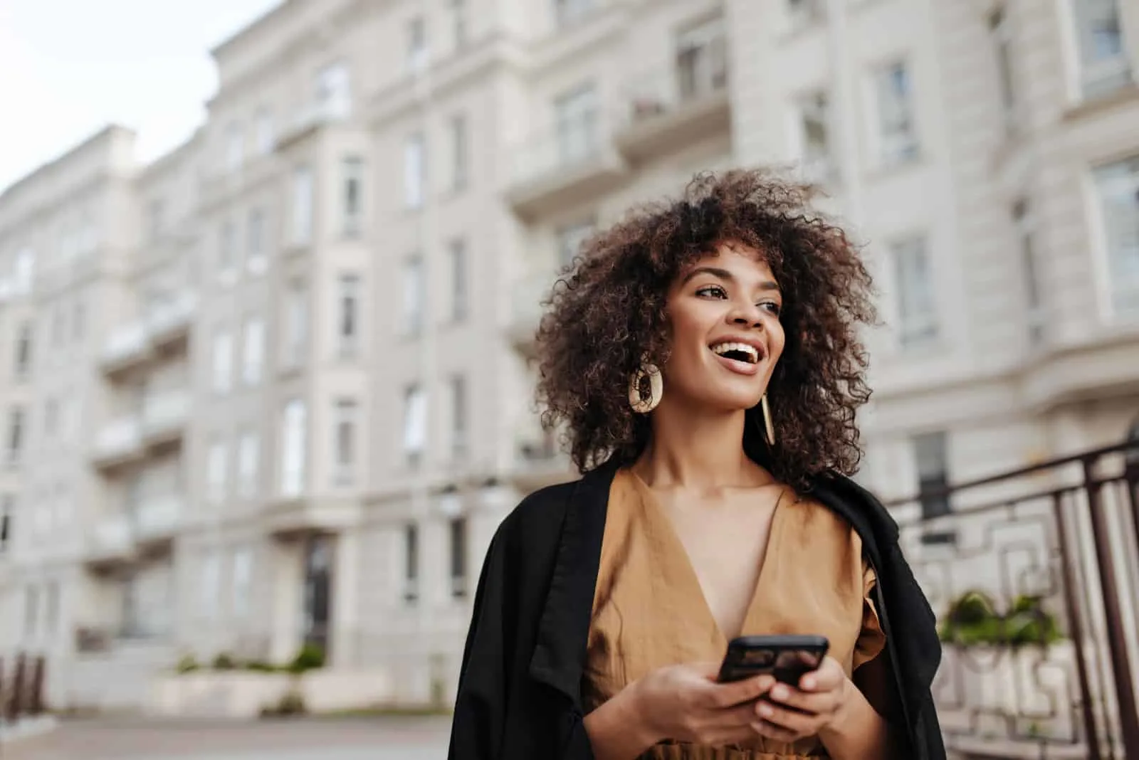 a smiling woman with frizzy hair stands on the street and buttons on the phone