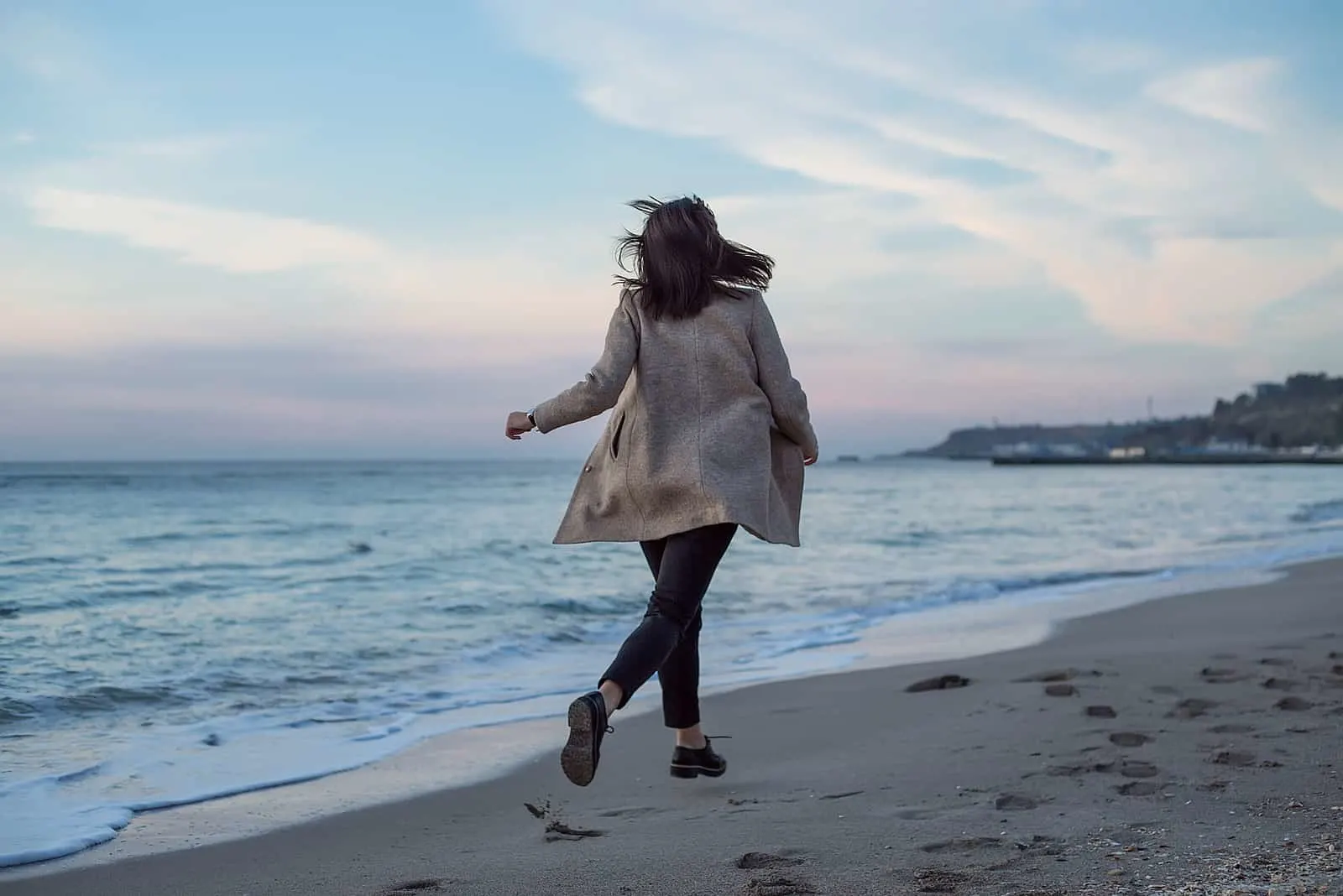 a woman in a long gray coat runs along the beach