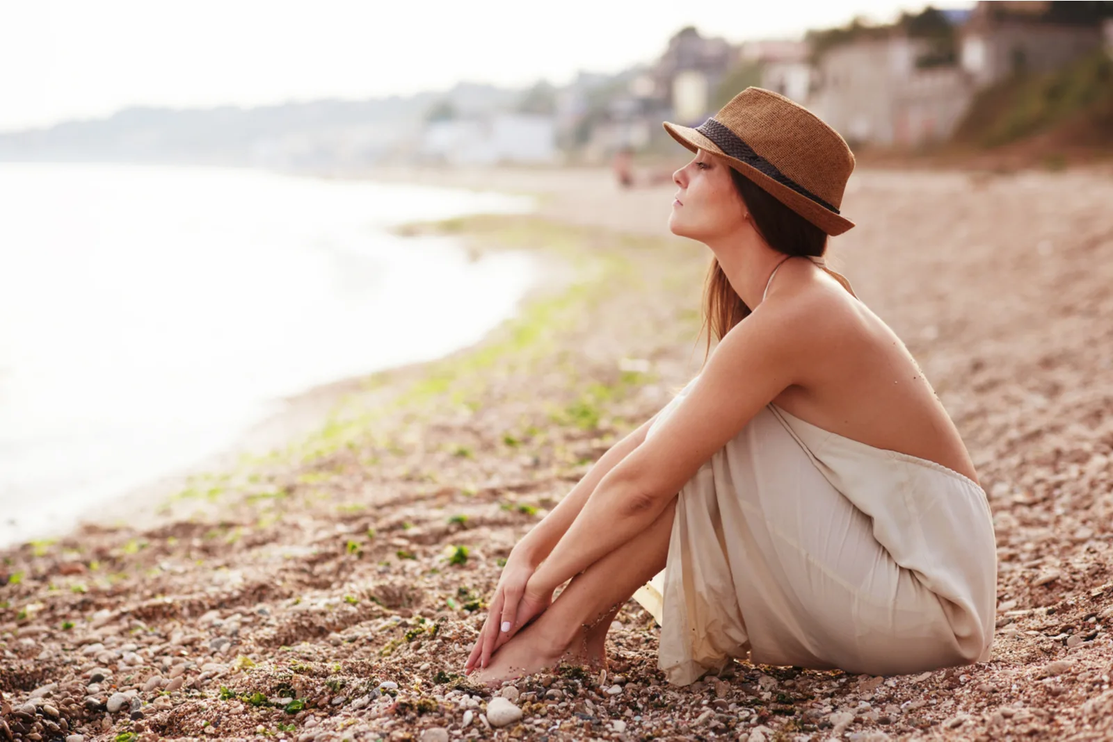 a woman with a hat on her head is sitting on the beach