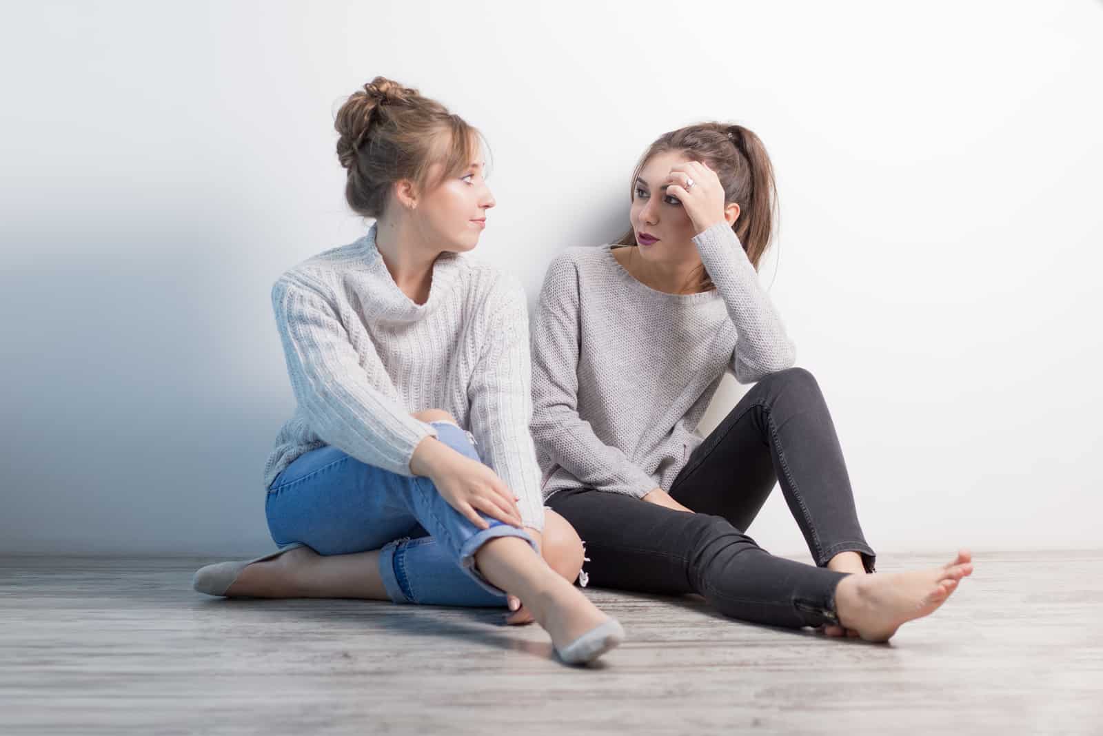 two friends sit on the floor and talk