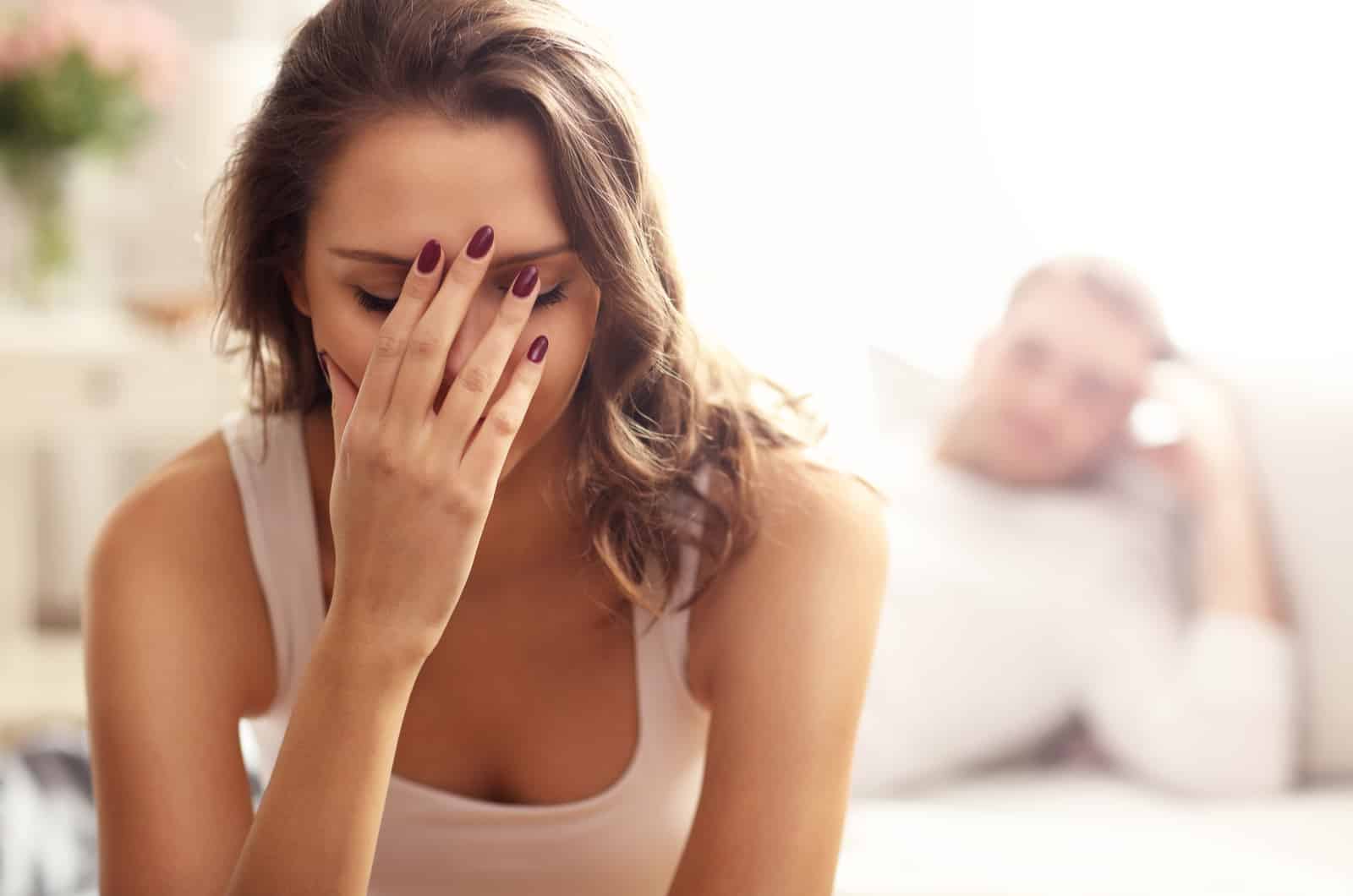 young woman sitting on bed with hand on face