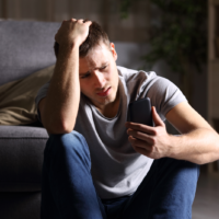 a man is sitting on the floor crying and holding a phone in his hand